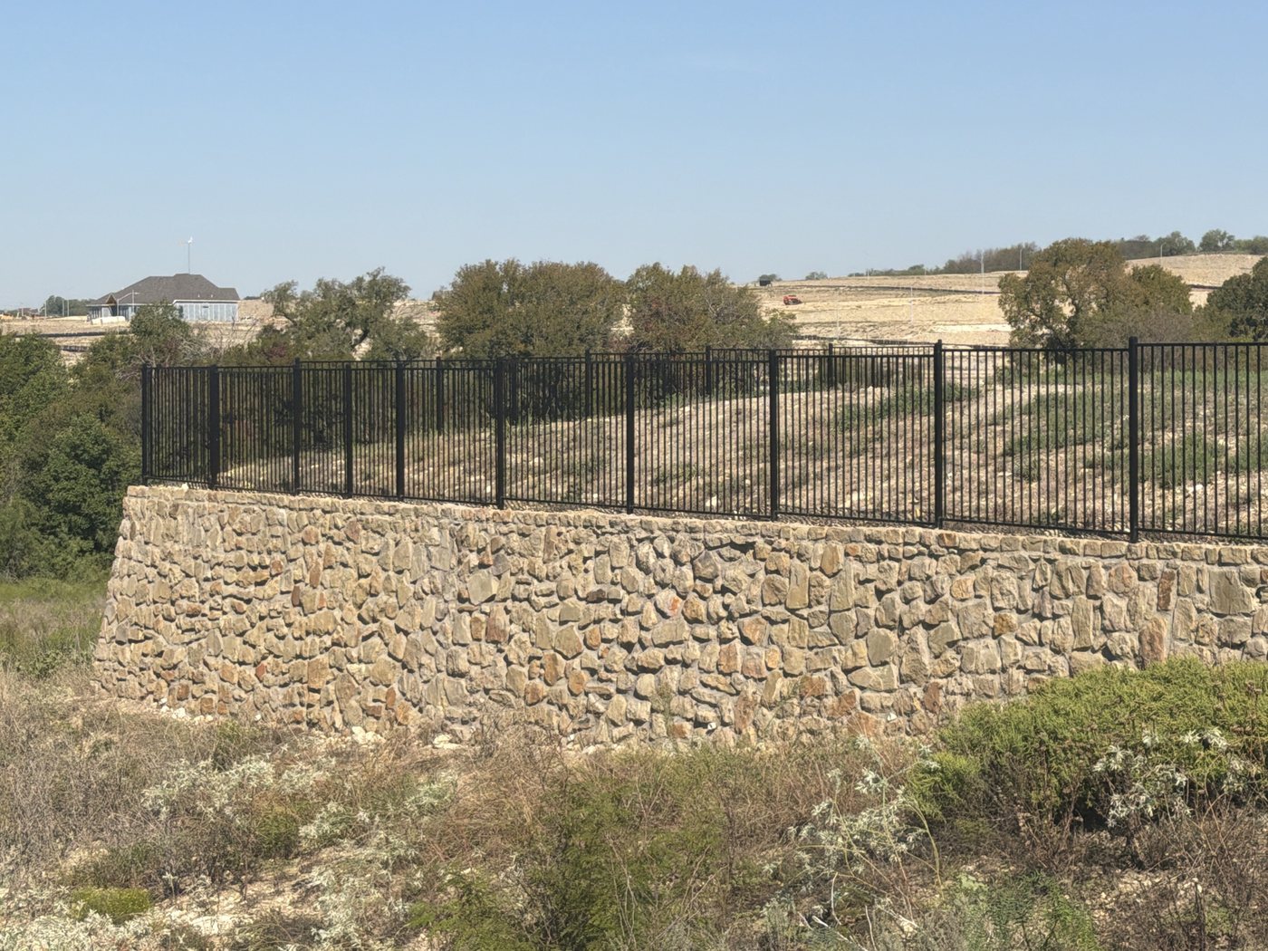 Stone wall with an iron fence on top at the edge of a greenbelt, Northpointe West, Fort Worth