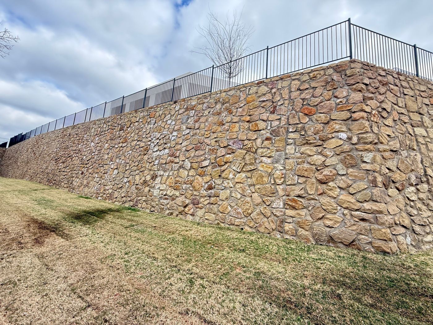Tall stone retaining wall with a fence along a greenbelt in Flower Mound