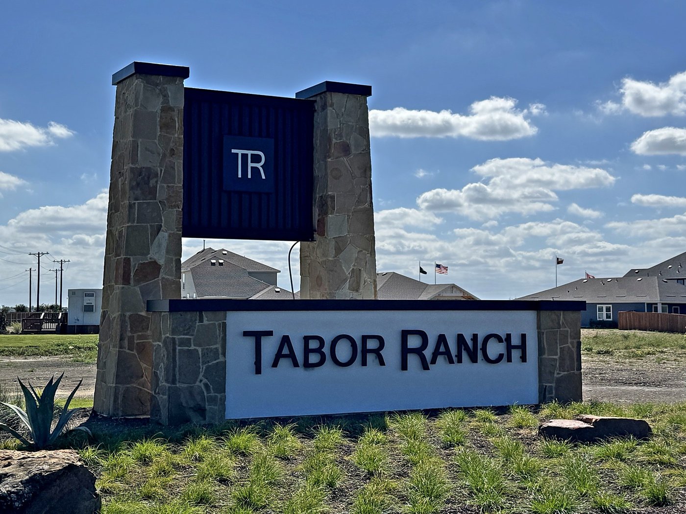 Stone entry monument with two tall stone towers carrying a steel sign panel in Denton