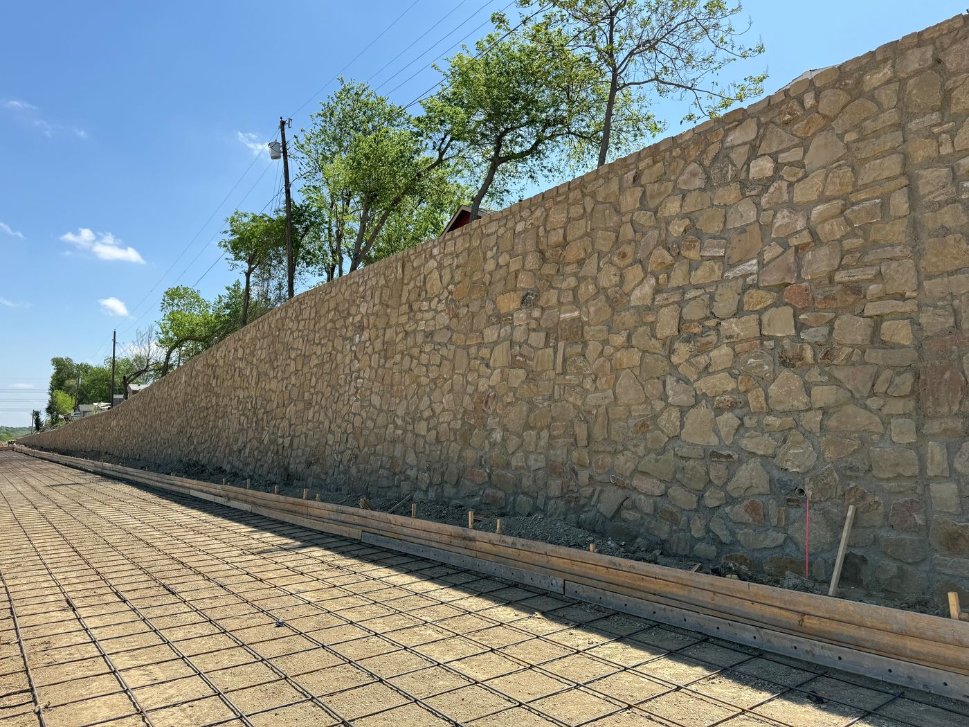Tall stone retaining wall along an industrial site in Irving